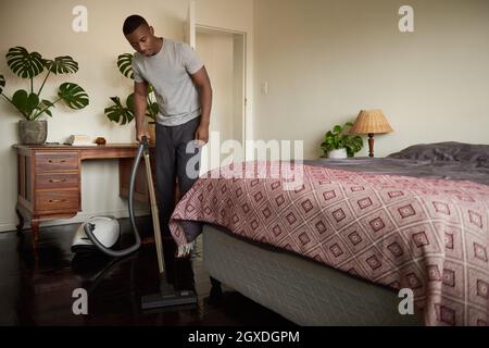 Junger afrikanischer Mann saugt zu Hause seinen Schlafzimmerboden Stockfoto
