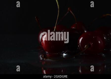 Kirschen, mit Wassertropfen auf schwarzem Hintergrund mit Spiegelung Stockfoto