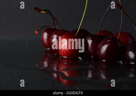 Kirschen, mit Wassertropfen auf schwarzem Hintergrund mit Spiegelung Stockfoto
