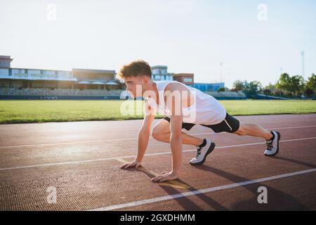 Seitenansicht männlicher Athlet in Sneakers, der in Startposition steht, bevor er im Sonnenlicht auf der Strecke trainiert Stockfoto