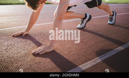 Crop männlichen Athleten in Turnschuhen in Startposition stehen vor dem Training auf der Strecke in Sonnenlicht Stockfoto