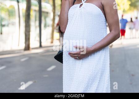 Cropped unkenntlich schwanger afrikanisch American trägt weißes Kleid beim Gehen auf der Straße Stockfoto