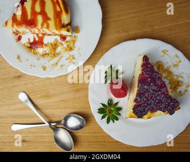 Set von Käsekuchen mit Erdbeer, zerbröselten Keksen, Erdbeersoße und zwei Löffeln auf Holzboden. Draufsicht Stockfoto