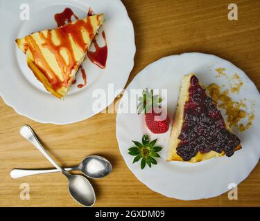 Set von Käsekuchen mit Erdbeer, Erdbeersoße, zerbröckeltem Gebäck und zwei Löffeln auf Holzboden. Draufsicht Stockfoto