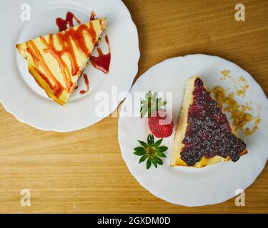 Set von Käsekuchen mit einer Erdbeere, Erdbeersoße tropfen und zerbröckelten Keksen auf Holzhintergrund. Draufsicht Stockfoto