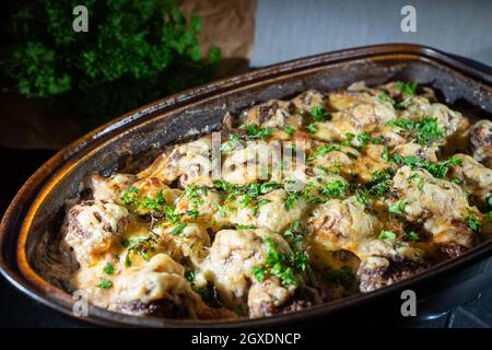 Gratinierte Fleischbällchen in einem rustikalen Bräter mit frischer Petersilie auf der Oberseite und dem Kraut im Hintergrund Stockfoto