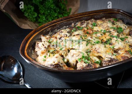 Gratinierte Fleischbällchen in einem rustikalen Bräter mit frischer Petersilie auf der Oberseite und dem Kraut im Hintergrund Stockfoto