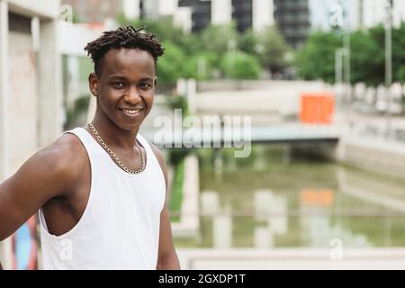 Positiver afroamerikanischer Mann, der hell lächelt, während er auf der Brücke steht und die Kamera anschaut Stockfoto