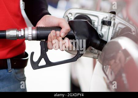 Tankstellenmitarbeiter in roter Uniform füllen Bronze Pickup LKW-Tank. Nahaufnahme Hand mit schwarzer Gaspumpendüse. Stockfoto