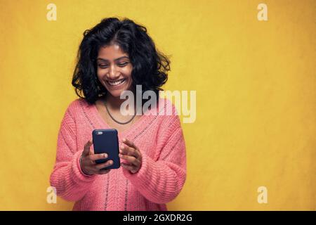 Schöne Sri Lanka Mädchen macht Technologie Posen mit gelb hell Hintergrund - Junge Frau nutzt Handy zu chatten und Messaging Stockfoto