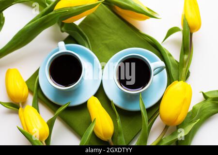 Zwei blaue Tassen Kaffee auf einem Tisch mit grünem Tuch und gelbe Tulpen Stockfoto