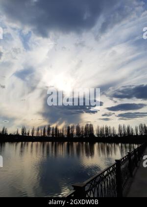 Die Sonnenstrahlen durchdringen die Frühlingswolken bei Sonnenuntergang über dem Stadtersee. Stockfoto