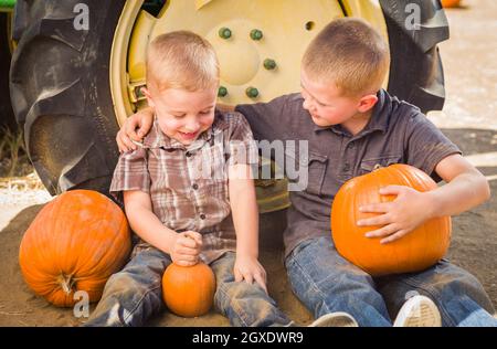 Zwei Jungs sitzen gegen einen Traktor Reifen Holding Kürbisse und reden in rustikalem Ambiente. Stockfoto