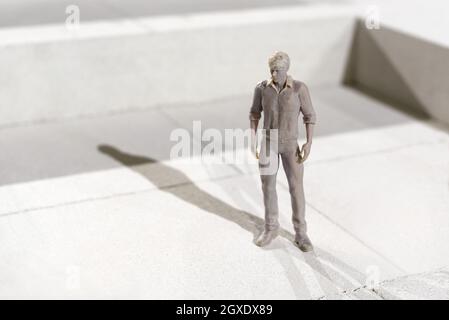 Miniatur 3d gedruckte monochrome Figur eines Mannes in Freizeitkleidung, der auf Fliesen steht und mit Copyspace einen Schatten im Sonnenlicht wirft Stockfoto