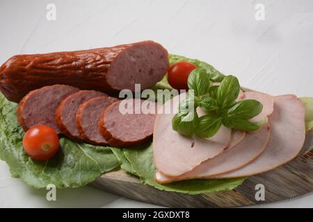 In Scheiben geschnittenes, würziges Rinderfleisch/Schweinefleisch und putenpastrami-Scheiben. Mit Salatblatt und Basilikum, Kirschtomaten. Stockfoto