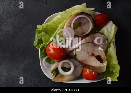 Scheiben von kalt geräuchertem Makrelenfisch, mit Kirschtomaten und roten Zwiebeln auf Salatblättern. Stockfoto