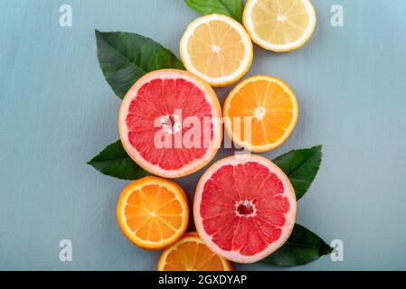 Draufsicht auf bunte Fruchtscheiben mit Zitrusblättern-Bordüre. Sommerliches tropisches Saftkonzept mit Zitrone, Grapefruit und Orange auf Vintage-Blau Stockfoto