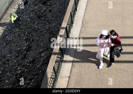 Zwei asiatische Frauen gehen am 28. September 2021 in London, Großbritannien, zu Fuß, während sie ein Mobiltelefon an der South Bank betrachten. Kredit: SMP NACHRICHTEN / Alamy Live Nachrichten Stockfoto