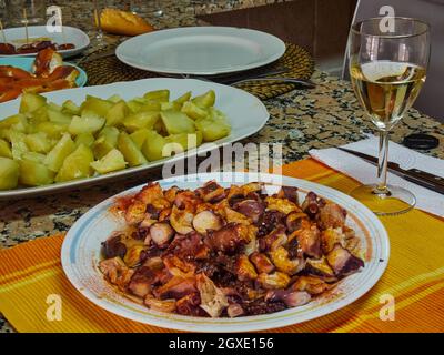 Octopus mit Paprika und Olive Oli namens 'Pulpo a feria, typisch für Galicien, Spanien', Kartoffeln, mehreren Tapas und einem Glas Weißwein Stockfoto