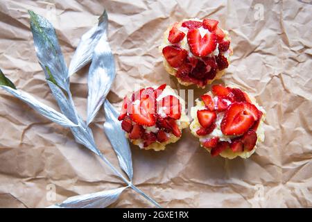 Schöne kleine Kuchen mit Erdbeeren zusammen mit einem Zweig auf Kraftpapier. Stockfoto