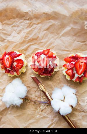 Schöne kleine Kuchen mit Erdbeeren zusammen mit einem Zweig der Baumwolle liegt auf Kraftpapier. Stockfoto