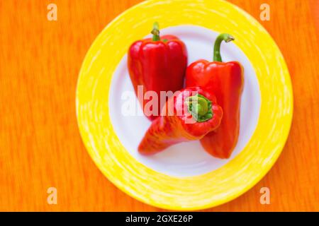 Drei rote Paprika auf einem bunten Teller Nahaufnahme. Stockfoto