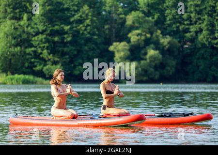 Zwei junge Frauen machen gemeinsam Yoga auf dem Brett in einer Mitte des Sees. Hochwertige Fotos Stockfoto