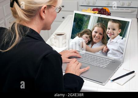 Frau in der Küche mit Laptop Siehe Freunde und Familie. Der Bildschirm kann ganz einfach für Ihre eigene Nachricht oder Ihr eigenes Bild verwendet werden. Bild auf dem Bildschirm ist mein Copyright Stockfoto