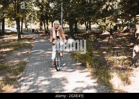 Älterer asiatischer Mann, der im Herbstpark Fahrrad fährt Stockfoto