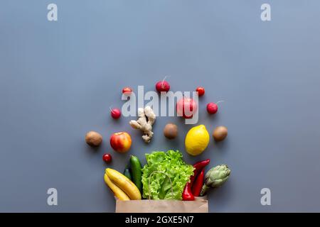 Gesundes und organisches Lebensmittelflay Lay-Konzept auf grauem Hintergrund. Öko Beutel mit Salatblättern, Äpfeln, Kiwi, Tomaten, Rettich, Zitrone, Gurke, Artike Stockfoto