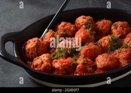 Boulettes de Poisson, gebratene Fischbälle in Tomatensauce in einer schwarzen Schale auf einem Betontisch mit Zutaten Stockfoto