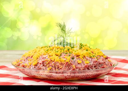 Traditioneller russischer Salat mit dem Namen Hering unter einem Pelzmantel. Traditionelle russische Küche präsentiert auf einem rustikalen Holztisch und einem hellen Pastell-BA Stockfoto