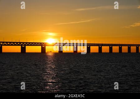 Sonnenuntergang mit der Sonne über und durch einen Abschnitt der Oresundbrücke am Aussichtspunkt bei Limhamn, Schweden, im Februar 2021. Der Himmel ist klar. Schiff sichtbar Stockfoto