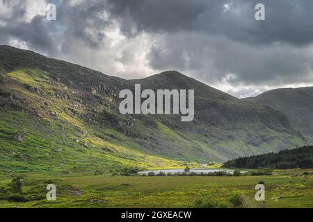 Kleiner See, Lough Gummeenduff im Black Valley, felsige Hügel der MacGillycuddys Reeks Berge, beleuchtet von Sonnenlicht, Ring of Kerry, Irland Stockfoto