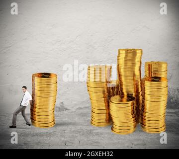 Geschäftsmann bewegt einen Stapel von goldenen Münzen zu einer Gruppe von Geld. Konzept der Schwierigkeit, Geld zu sparen Stockfoto