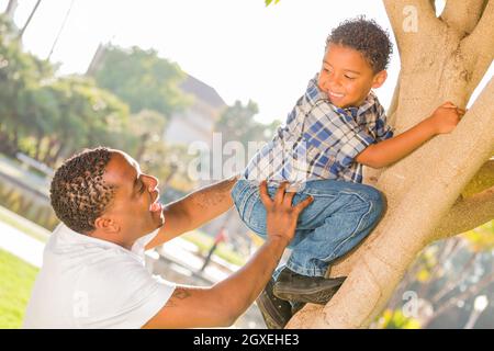 Happy Mixed Race Vater helfen Sohn klettert einen Baum im Park. Stockfoto