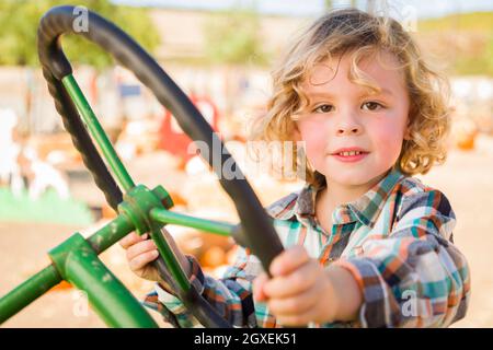 Entzückende junge auf einen alten Traktor in einer rustikalen Outdoor-Herbst-Umgebung zu spielen. Stockfoto