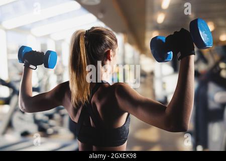 Eine athletisch muskulöse Frau trainiert Bizeps mit Kurzhanteln im Fitnessstudio Stockfoto