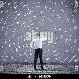Verwirrt Geschäftsmann auf der Suche einer Wand mit Richtungspfeilen. Konzept der Verwirrung Stockfoto