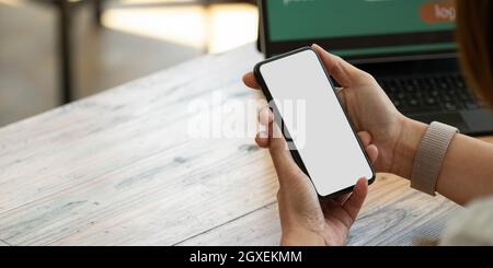 Nahaufnahme der Hände mit einem mobilen Smartphone mit leerem Bildschirm und Notebook und Laptop. Stockfoto