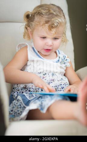 Entzückende Blonde behaarte Blue Eyed kleines Mädchen ihr Buch auf dem Stuhl. Stockfoto