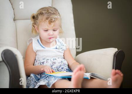 Entzückende Blonde behaarte Blue Eyed kleines Mädchen ihr Buch auf dem Stuhl. Stockfoto