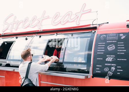 Ein junger Mann kauft Fast Food, während ihm ein LKW-Angestellter zwei Burger übergibt Stockfoto