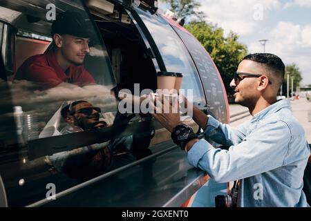 Typ in Freizeitkleidung und Sonnenbrille, der am Sommertag zwei Getränke im Street Food Truck kauft Stockfoto