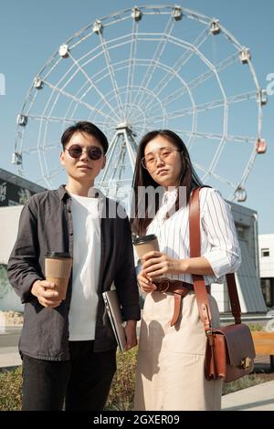 Junge chinesische Studenten stehen gegen das Riesenrad und schauen auf die Kamera Stockfoto