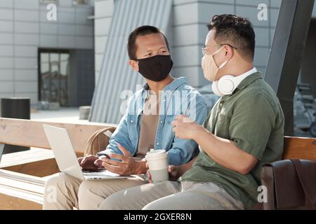 Zwei chinesische Geschäftsleute in Schutzmasken, die bei einem Treffen im Freien diskutieren Stockfoto