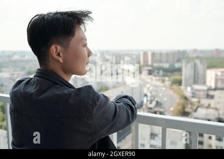 Rückansicht einer jungen Chinesin, die auf dem Balkon vor dem Stadtbild steht Stockfoto