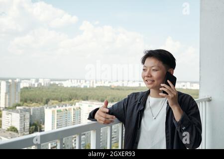Glückliche junge asiatische Geschäftsfrau, die auf dem Balkon auf dem Handy spricht Stockfoto