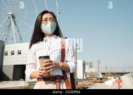 Junge Geschäftsfrau in Schutzmaske mit Kaffeepause im Freien Stockfoto