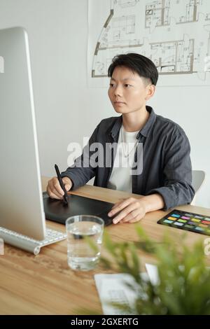 Junger chinesischer Designer mit Stylus-Stift-Zeichnung auf Tablet-Display vor dem Computer Stockfoto